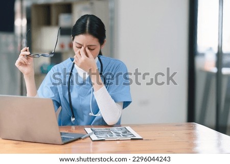 Professional millennial female doctor or nurse working on laptop computer and clipboard with a tense expression while sitting at a desk Royalty-Free Stock Photo #2296044243