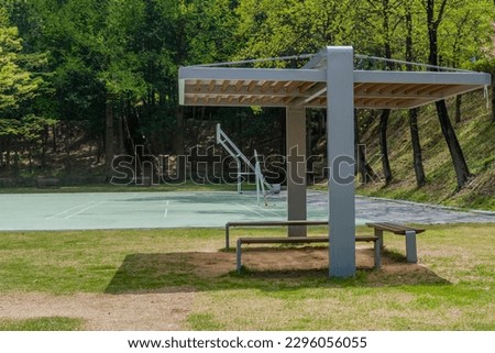 Closeup of covered park benches with basketball court in background.