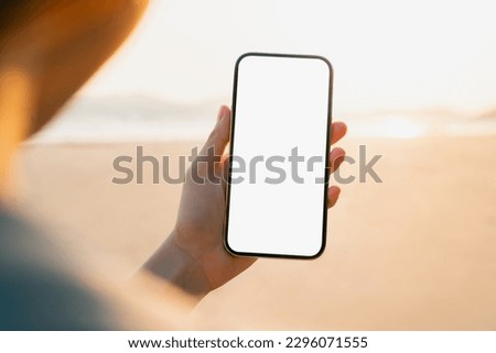 Hand holding smartphone on the beach, mobile mockup of blank screen, Take your screen to put on advertising. Summer vacation concept. Royalty-Free Stock Photo #2296071555