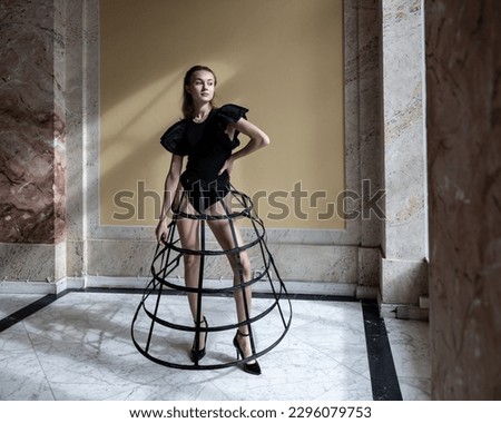 A young model in a skirt frame stands by the window in the sunlight among the marble walls