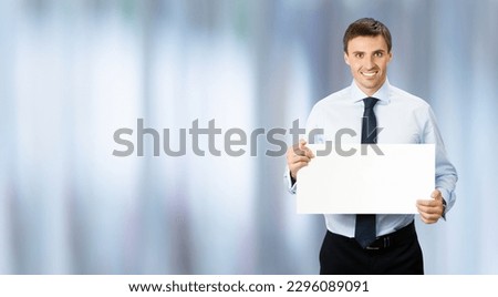 Image of business man professional bank manager in confident cloth, wear shirt, necktie tie. Standing businessman hold, show empty white banner sign board. Blurred office background.