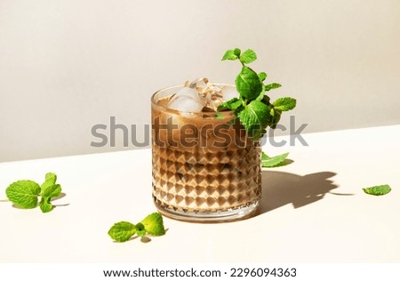 Mint White Russian alcoholic cocktail drink with vodka, coffee liqueur, mint schnapps, cream and ice on beige background, hard light, shadow pattern, copy space