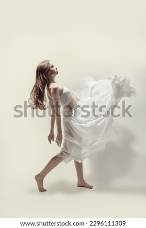 A young graceful ballerina in a delicate white dress dances with expression. Full-length studio portrait. Modern ballet dancer. Choreography. 
