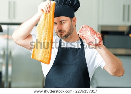 Man chef cooker hold fish and meat, salmon and beef. Male chef in chefs uniform with raw meat beef and fish salmon fillet. Chef man cooking raw meat beef and fish salmon fillet on kitchen.