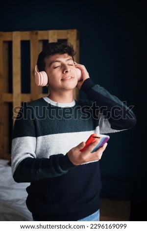 young latin homosexual man with headphones listen music on mobile phone at home in Mexico, Hispanic LGBT community in Latin America