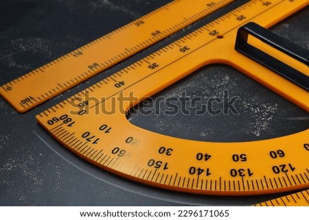 Protractor and ruler with measuring length and degrees markings on blackboard, closeup