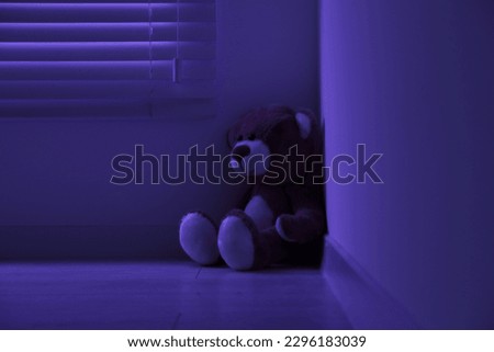 Cute lonely teddy bear on floor in corner of dark room Royalty-Free Stock Photo #2296183039