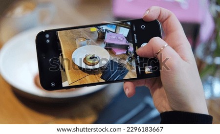 Closeup of women's hands making photo of sweet dessert on mobile phone while sitting in comfortable restaurant, female taking pictures with cell phone camera of delicious pastry during rest in cafe