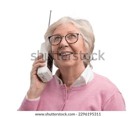 Happy senior woman talking with an old cordless telephone, she is smiling and listening
