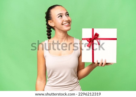Young Arab woman holding a gift over isolated background looking up while smiling