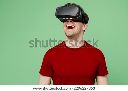 Young surprised caucasian amazed happy fun man he wears red t-shirt casual clothes watching in vr headset pc gadget isolated on plain pastel light green background studio portrait. Lifestyle concept