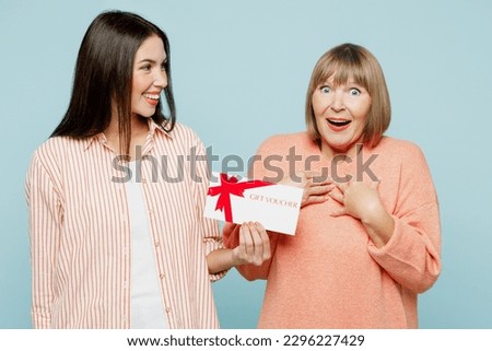Surprised fun elder parent mom with young adult daughter two women together wears casual clothes hold store gift certificate coupon voucher card isolated on plain blue background. Family day concept
