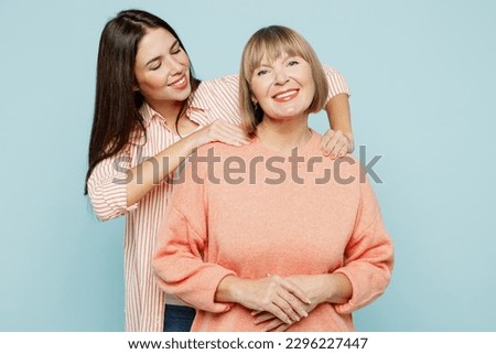 Elder retired tired parent mom with young adult daughter two women together wear casual clothes massaging mother's shoulders make to relax isolated on plain blue cyan background. Family day concept Royalty-Free Stock Photo #2296227447