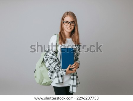 Smiling little schoolgirl 11-13 years old with backpack holding book isolated on gray background studio portrait. The concept of children's lifestyle. Education at school. Royalty-Free Stock Photo #2296237753