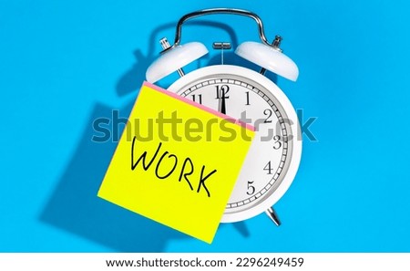 White alarm clock and a sticker with the inscription Work on a blue background.