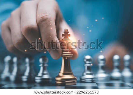 Businessman holding golden king chess in front of silver pawn chess on chessboard for business strategy and leadership assignment concept. Royalty-Free Stock Photo #2296251573