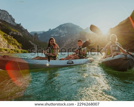 A group of friends enjoying fun and kayaking exploring the calm river, surrounding forest and large natural river canyons during an idyllic sunset. Royalty-Free Stock Photo #2296268007