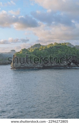 The scenery of a cliffside coastline with lush green vegetation on top of the cliff and cloudy blue sky background