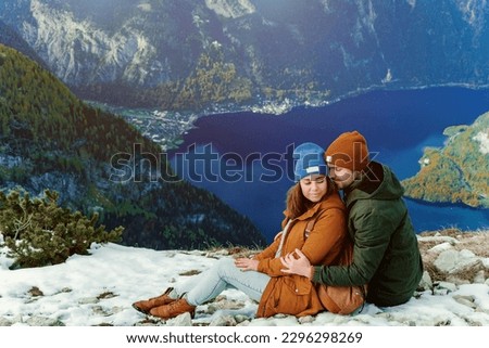 Lovely family couple sitting on moutain peak with beautiful background and taking hugs. Wonderful picture with copy space. Five fingers view point near Hallstatt village in Austria. Amazing valley.
