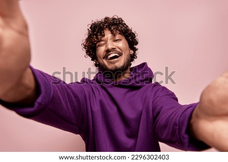 Low angle view of happy young Indian man making selfie against pink background Royalty-Free Stock Photo #2296302403