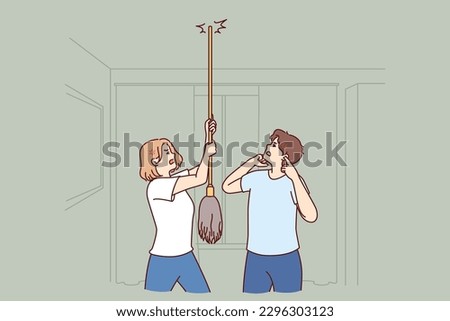 Young couple bangs on ceiling with mop urging neighbors to stop party or turn off loud music. Angry men and women use mop suffer from noisy neighbors not respecting rules of living together Royalty-Free Stock Photo #2296303123