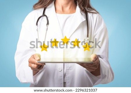 Medical services rating concept. Unrecognizable mature female doctor holding digital tablet with five stars icons above, blue studio background, cropped