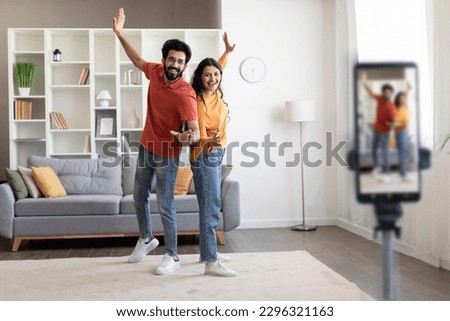 Happy Young Indian Couple Dancing At Camera While Recording Video At Home, Positive Eastern Spouses Creating Content For Social Networks, Using Smartphone On Tripod In Living Room, Copy Space