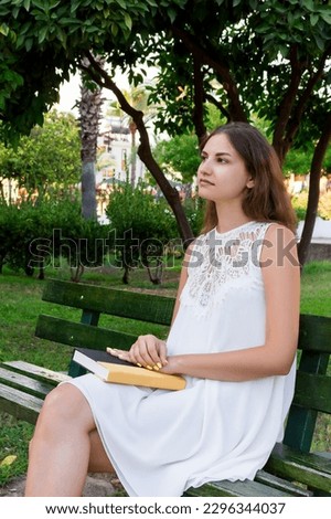 Young woman is holding a book and dreaming about something outside.