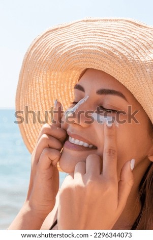 Smiling woman in hat is applying sunscreen on her face. Indian style.