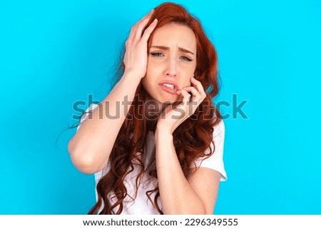 Gloomy Young redhead woman wearing white T-shirt over blue background , hiding face with hands pouting and crying, standing upset and depressed complaining about job problem. Royalty-Free Stock Photo #2296349555
