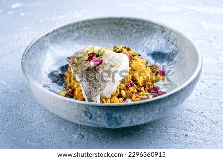 Modern style traditional sauteed skrei cod fish filet with skin in a bed of Persian jeweled saffron rice pilaw served in ceramic design bowl as close-up 