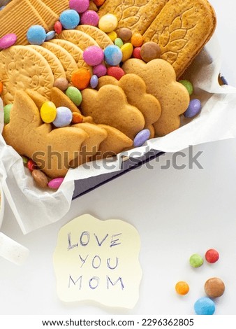 Assorted cookies and candies in the basket with Love you mom note. Mothers Day concept. Handmade care package, seasonal gift box with candies, dragee and cookies for mother on Valentines or Womens Day