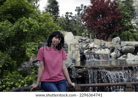 Photo of a mature woman, in the park alone breathing fresh air and admiring the flowers and the waterfall.