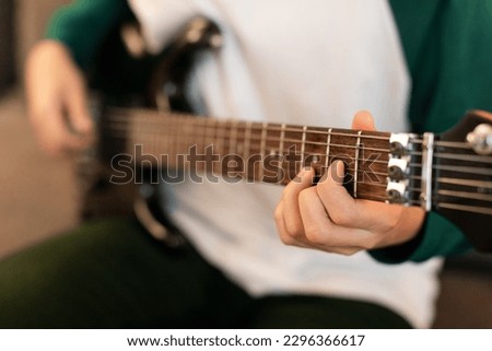 Musical Talent. Closeup Of Guy's Hands Playing Chords On Electric Guitar, Holding Instrument And Touching Strings Sitting Indoor. Music Hobby And Leisure. Cropped Shot, Selective Focus Royalty-Free Stock Photo #2296366617