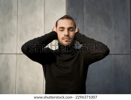 Young man with closed eyes covering his ears in an effort to block out the sound around him. Conceptual image of struggle with deafness and feeling disconnected from society Royalty-Free Stock Photo #2296371007