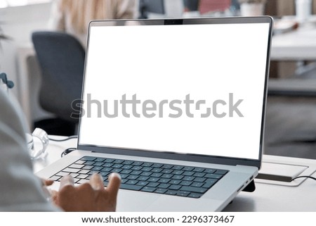 Young business woman working on laptop with blank copy space screen for ad app in modern busy office. Over shoulder view on businesswoman using touchscreen of a computer with white mockup monitor.