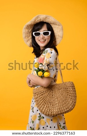 Studio portrait pretty young asian woman happy smile dressing springtime fashion with sunglasses, woven bag and holding tulip bouquet flower against yellow studio background. Person holiday concept.
