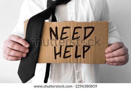 A disheveled business man holds up a cardboard sign with the words Need Help
