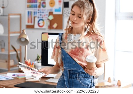 Female graphic designer with cup of coffee and color palettes in office
