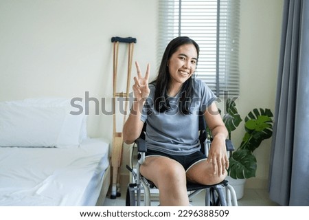 Portrait of Asian young amputee leg woman smiling, looking at camera. Attractive female having no leg feel happy and relax sit alone on wheelchair enjoy weekend activity lifestyles in morning at house