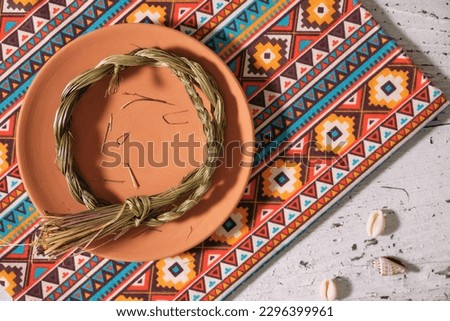 Sweetgrass braid (Hierochloe odorata), also called vanilla grass, on a clay plate, cloth with native american pattern. Overhead view.