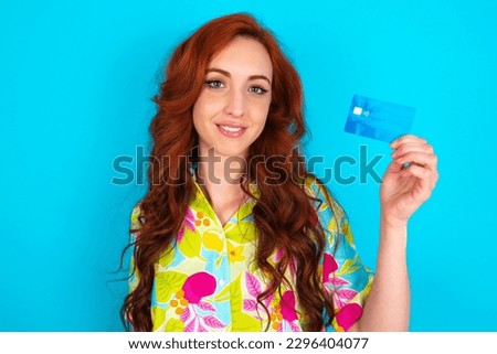 Photo of happy cheerful smiling positive Young redhead woman wearing colorful shirt over blue background recommend credit card