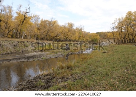 Dirt bike rider racing through river bed with autumn scenery in background