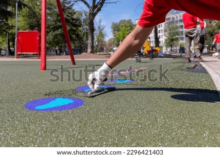 A mason hand with trowel  spreading and leveling soft rubber crumbs rubber mulch 
for children's playground. Outdoor soft coating and floor covering for sports. Rubber surface for safety. Royalty-Free Stock Photo #2296421403