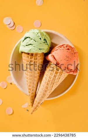 Various colorful ice cream scoops or balls with waffle cones on yellow background. Top view.