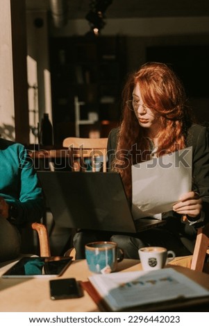 Front view shot of ginger businesswoman holding a document in the left hand and working on the lap top with the right