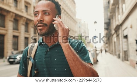 Close up, young man walks down the street on the old city and passing cars in the background and talks on the phone