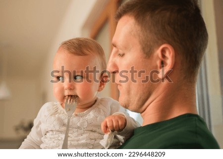 Handsome father is playing with his baby while looking her with the fork