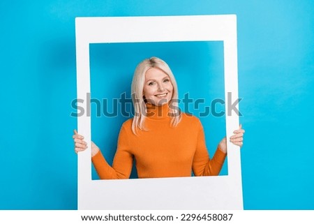 Portrait of good mood nice woman with blond hairstyle dressed orange sweatshirt hold photo frame isolated on blue color background