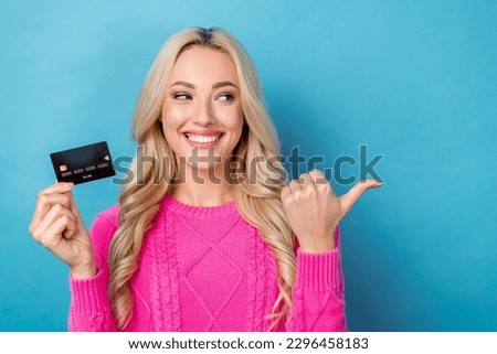 Photo of pretty thoughtful woman dressed knitted pullover holding credit card pointing thumb empty space isolated blue color background